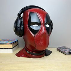 a deadpool mask with headphones is sitting on a table next to books and a cell phone