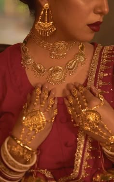 a woman wearing gold jewelry and holding her hands up to her chest with both hands