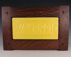 a yellow welcome sign in a wooden frame on a gray background with the word welcome