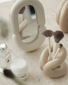 there are some makeup brushes in the cup and on the table next to it is a mirror