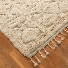 a white rug with tassels on top of it in the middle of a wooden floor