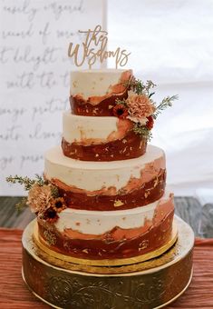 a three tiered wedding cake with flowers on the top is sitting on a gold platter