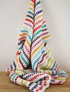 a multicolored crocheted blanket folded on top of a wooden table next to a white wall