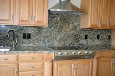 a kitchen with wooden cabinets and granite counter tops, stainless steel range hood over the stove