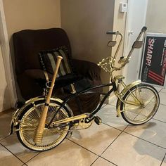 a gold bike parked in front of a brown chair and black couch with pillows on it