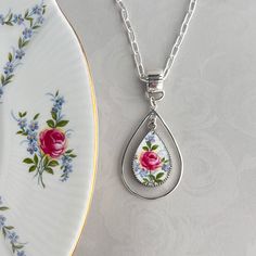 a white plate with a pink rose on it next to a silver and glass necklace