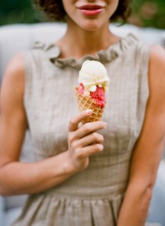 a woman is holding an ice cream cone with strawberries in it and looking at the camera