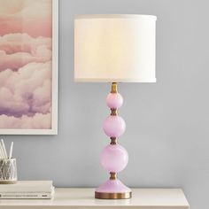 a pink lamp sitting on top of a table next to a white vase and book