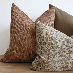 two pillows sitting on top of a wooden table next to each other, one brown and the other white