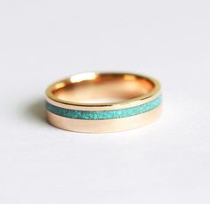 a wedding band with turquoise and gold inlays on the outside, set against a white background