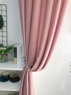 a pink curtain hanging on the side of a white wall next to a shelf with plants