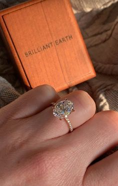 a woman's hand with a ring on it and an orange box in the background