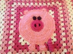 a crocheted pig pillow on top of a pink and white checkered blanket