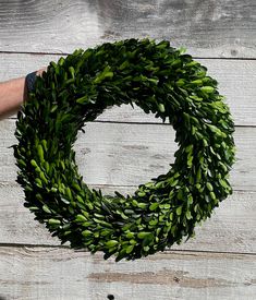 a hand holding a wreath on top of a wooden table next to a white wall