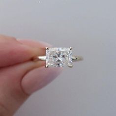 a person is holding an engagement ring with a princess cut diamond in it's center