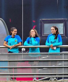 three girls in blue shirts are standing on a metal fence and looking at the camera