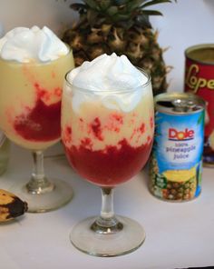 two glasses filled with desserts next to cans of cookies and pineapples on a table