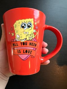 a hand holding a red coffee mug with an image of a cartoon character on it