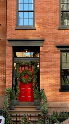 a red fire hydrant sitting in front of a brick building with wreaths on it