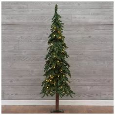 a small christmas tree with lights on it in front of a wooden wall and floor