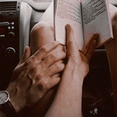 two hands on the steering wheel of a car while holding an open book in front of them