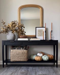 a black console table with some pumpkins on it and a mirror in the background