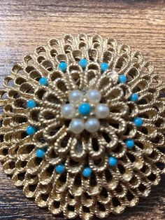 a brooch with pearls and blue beads on top of a wooden table next to a pair of scissors