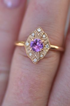 a close up of a person's hand holding a ring with a purple stone