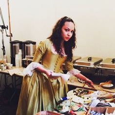 a woman dressed in an old fashioned dress is preparing food at a table with other items