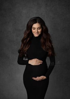 a pregnant woman in a black dress poses for the camera with her hands on her belly