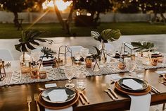 a long table with place settings and plates on it, in front of the sun