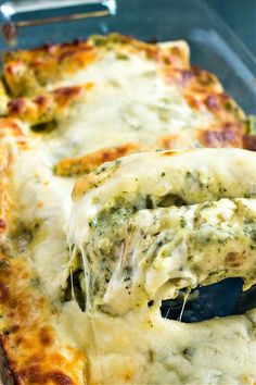 a cheesy pizza with spinach and cheese is being lifted from the casserole dish