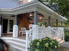 a porch with white railings and green plants on the front steps, next to a brick house