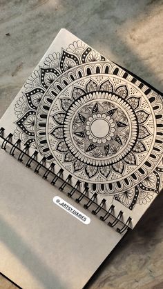 a notebook with an intricate design on the cover sitting on top of a wooden table