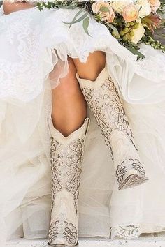 a woman in cowboy boots holding a bouquet with flowers on her wedding dress and veil