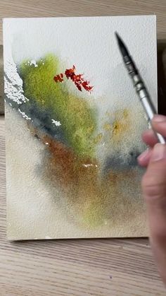 a person is holding a paintbrush in front of a piece of paper with watercolors on it