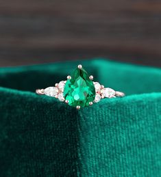 an emerald colored ring with two diamonds on it's sides, sitting in a green velvet box