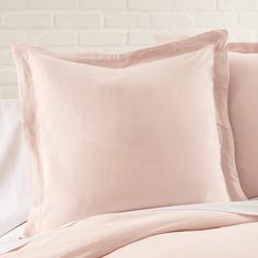 a bed with pink sheets and pillows in front of a white brick wall behind it