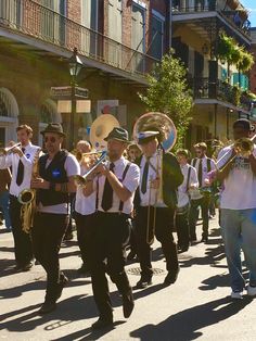 a group of people marching down the street with musical instruments in their hands and wearing white shirts