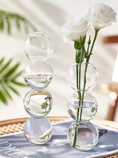 two clear vases with flowers in them sitting on a table next to a cell phone