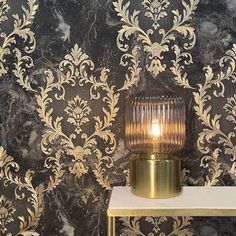 a table with a lamp on it next to a wallpapered background that looks like damask