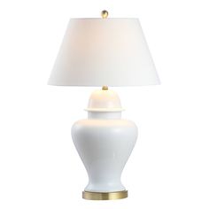 a white lamp with a gold base and a white shade on the top is sitting against a white background