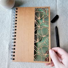 a hand holding a pen next to a notebook with an intricate design on the cover