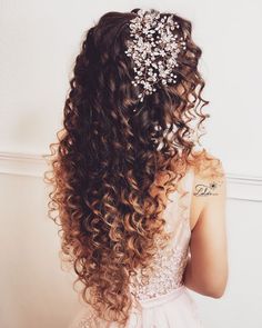 the back of a woman's head with long curly hair and flowers in her hair