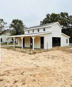 a white horse barn sitting in the middle of a dirt field