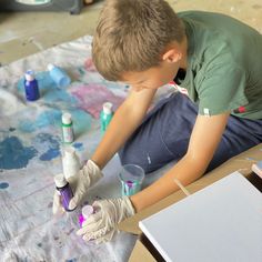 a young boy is painting on the floor with paintbrushes and tubes in front of him