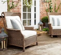 two wicker chairs sitting on top of a patio next to a brick wall and windows