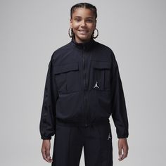 This jacket is a modern silhouette made of woven nylon for lightweight warmth featuring logo taping trim. The flattering boxy cut creates a cropped look with a full-zip closure for easy layering. Cargo pockets on the chest have hook-and-loop flap closures to help secure small items and on-seam pockets at the sides provide extra spots to stash smaller items. Dropped shoulders create a relaxed fit and the elasticized cuffs and hem help secure the jacket in windy conditions. Pair with the Jordan Jumpman Woven Taping Pants for a coordinated look. Sporty Black Track Jacket With Side Pockets, Black Sporty Track Jacket With Side Pockets, Sporty Windbreaker With Cargo Pockets For Streetwear, Black Sports Outerwear With Side Pockets, Functional Track Jacket With Side Pockets For Streetwear, Black Sporty Windbreaker With Side Pockets, Black Track Jacket With Side Pockets For Streetwear, Sporty Windbreaker With Cargo Pockets For Fall, Black Spring Windbreaker With Side Pockets