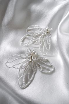 two white beaded brooches sitting on top of a white satin material sheet