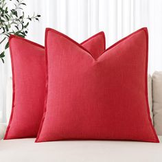 two red pillows sitting on top of a white couch next to a potted plant